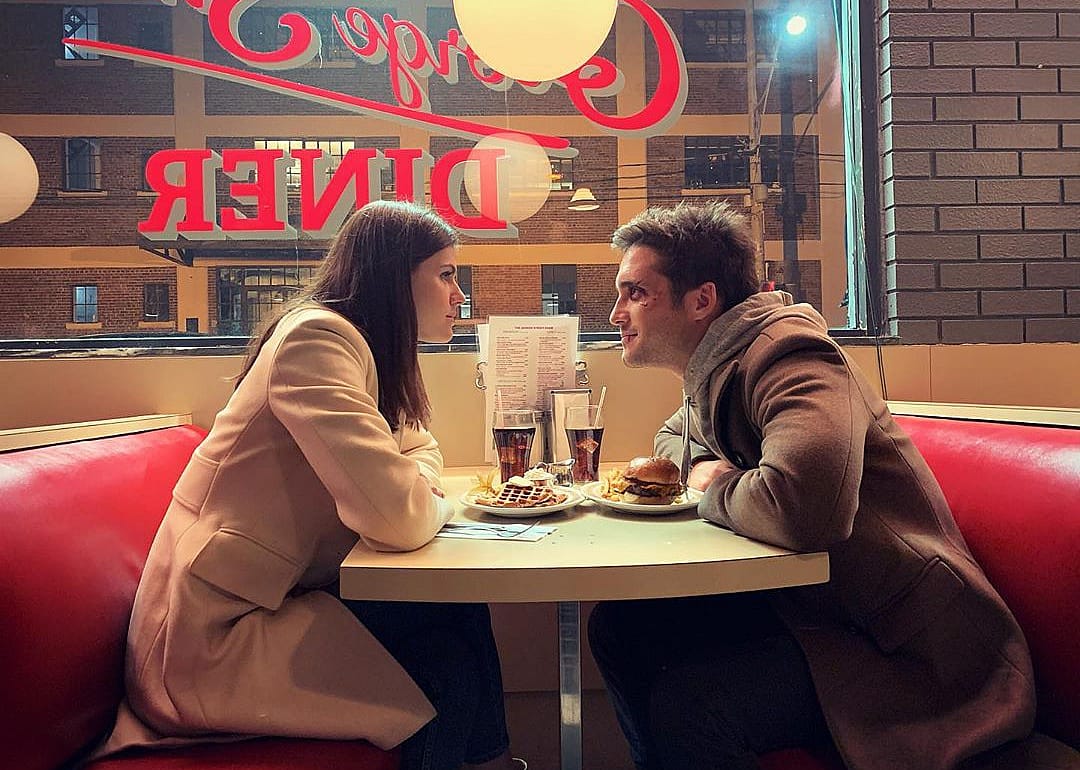 Two young adults sitting across from each other in a diner booth.
