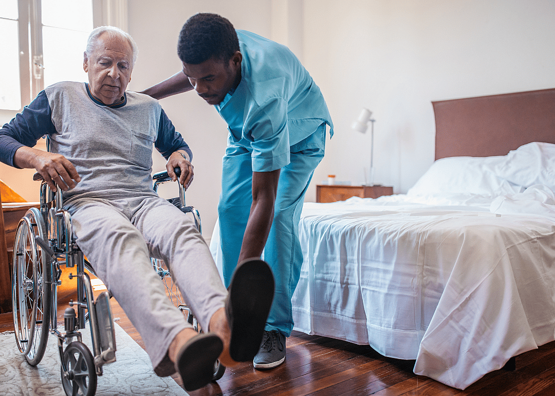 An orderly helping a man in a wheelchair put on shoes.