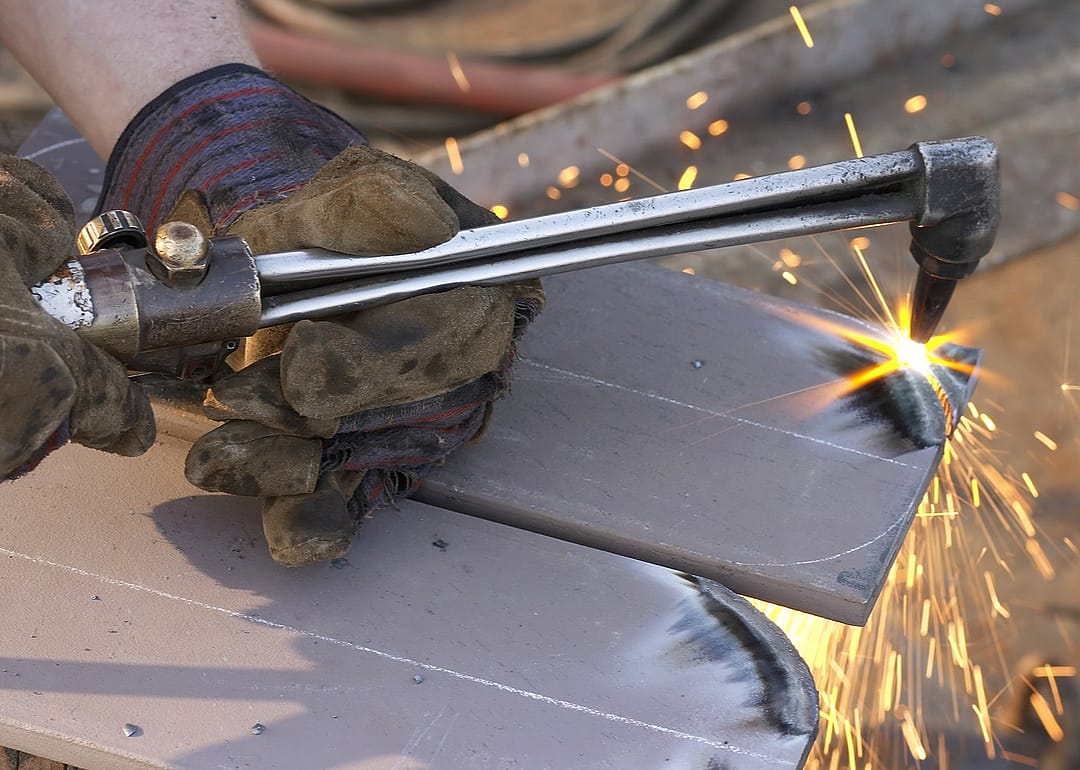 A worker uses a welding torch on a piece of metal.