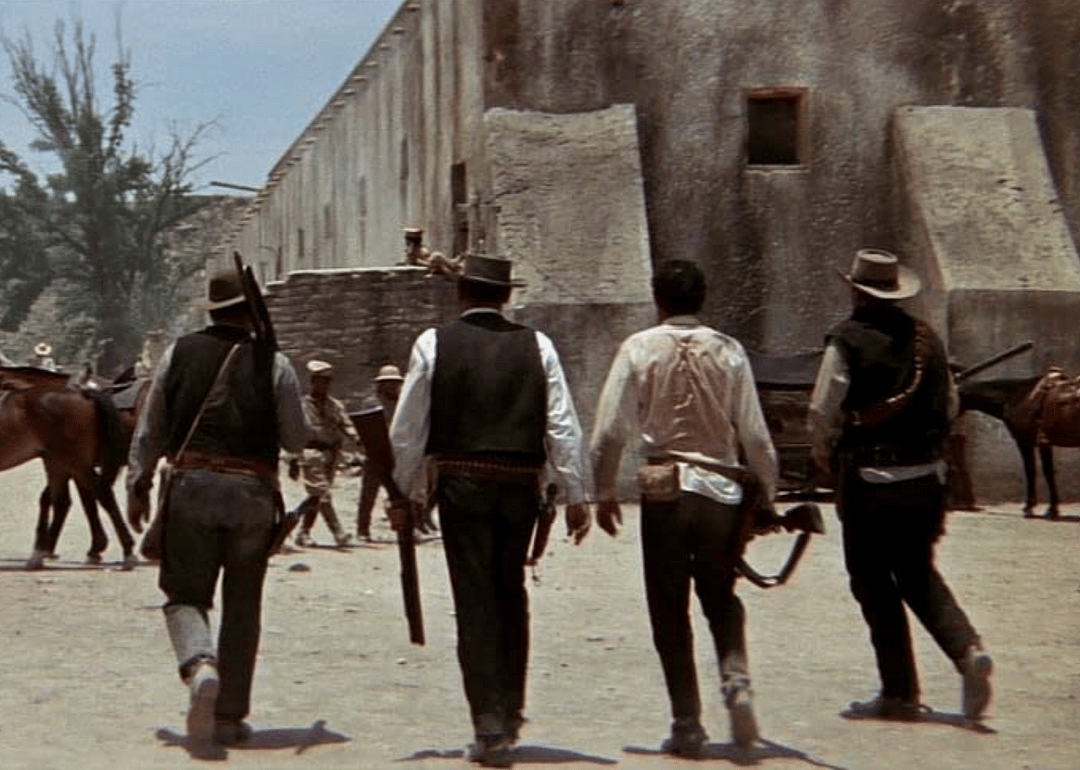 Four western men with guns walking down a street.