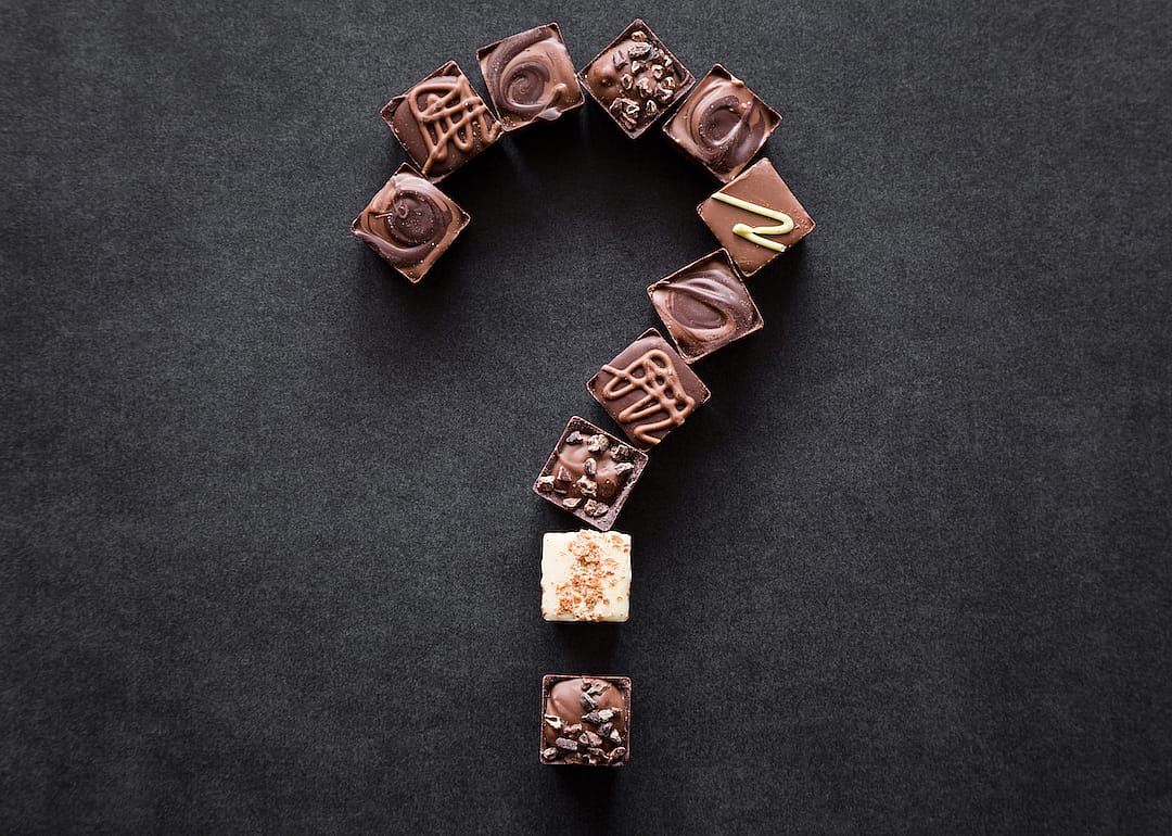 Question mark created from pieces of chocolate candies on a dark table.