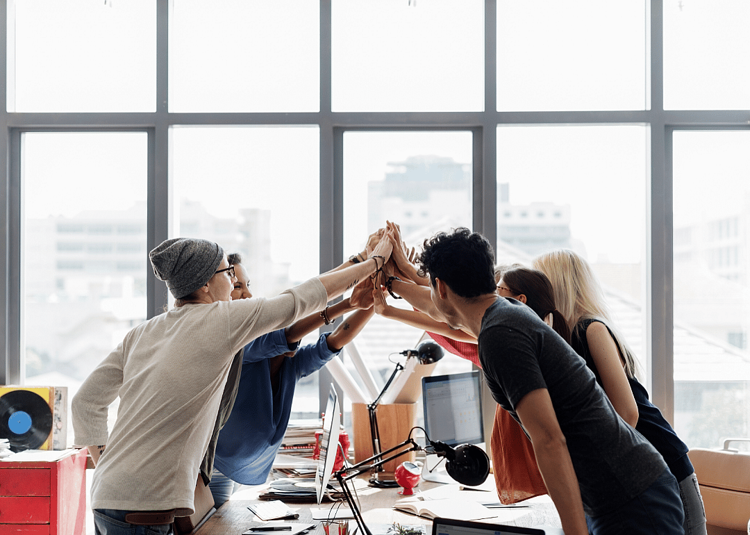 Employees giving a group high five in a brightly lit office.
