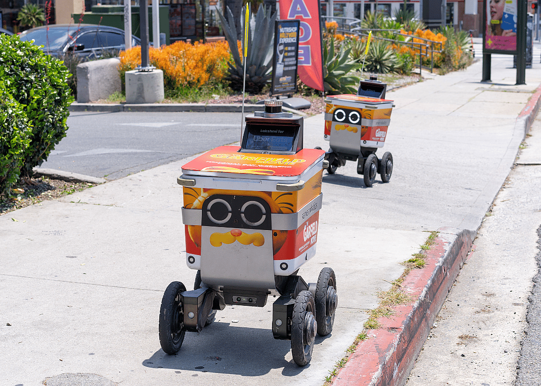 Two delivery robots in the city going down a sidewalk.