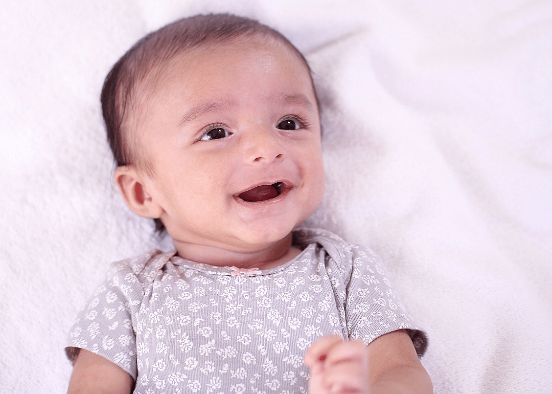 Smiling baby lying on back on white blanket.
