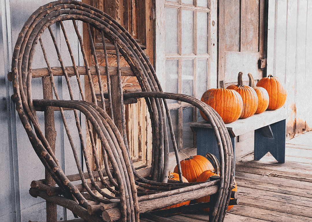 A rustic wooden rocking chair and pumpkins on a porch.