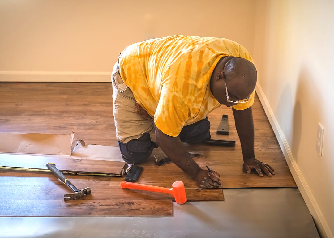 A carpenter working to install a new laminated floor in a residential home