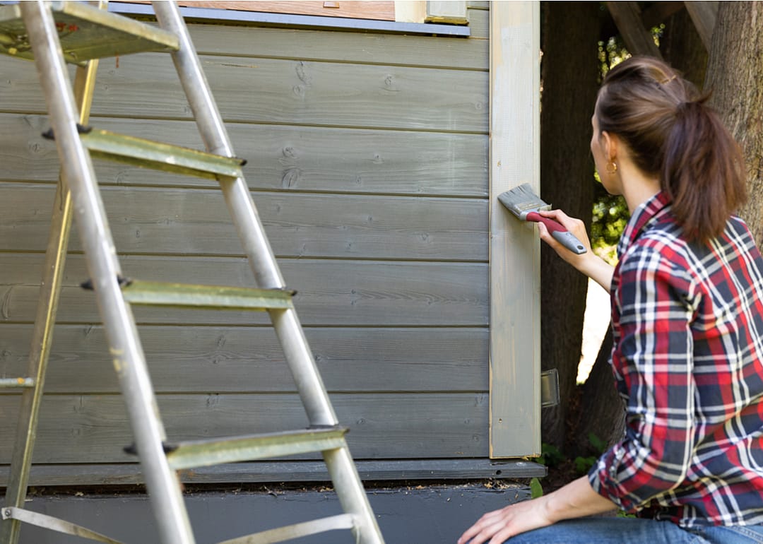 A woman painting the exterior wall of a wooden house