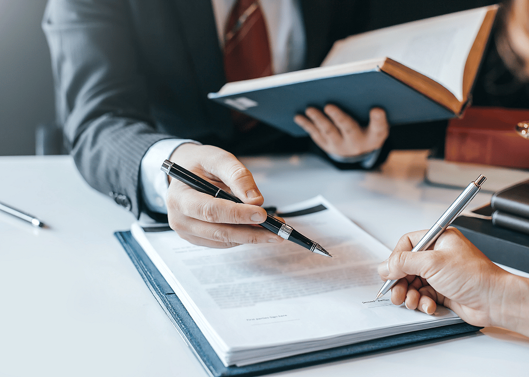 A close up of a lawyer's hands showing a client where to sign a document. 