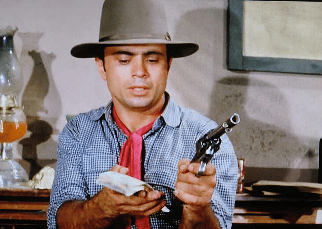 A man in a cowboy hat holding money and a pistol.