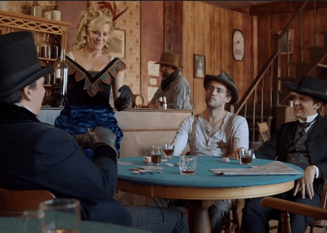 Men at a poker table and a woman serving drinks at a saloon.