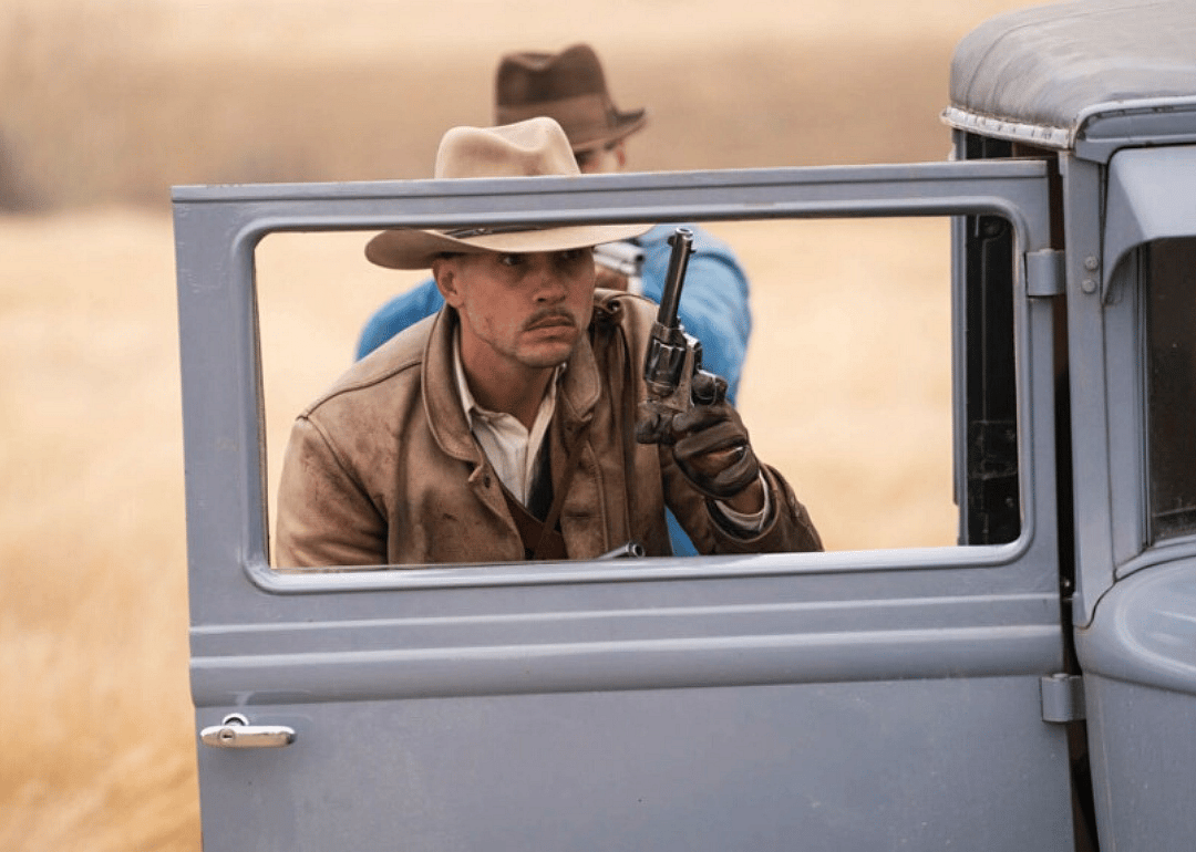 A man with a pistol behind an open car door.