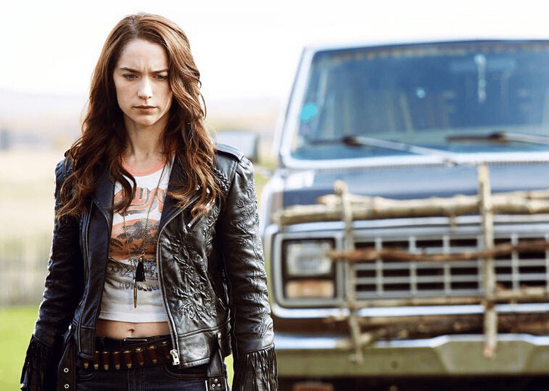 A woman in a leather jacket in front of a pick up truck.