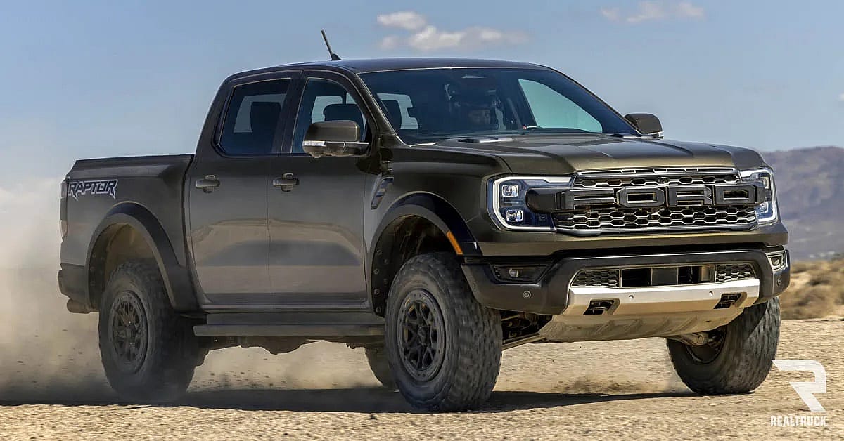 A black Ford Ranger Raptor driven in a sandy wide lot.