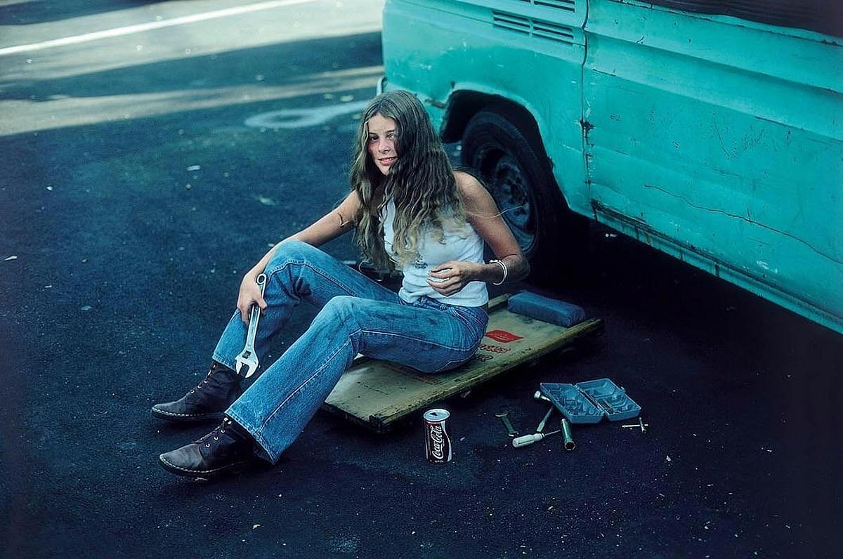 A woman in jeans and boots working on her blue VW van