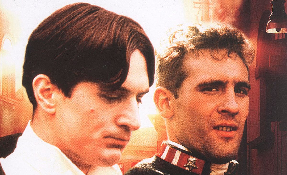 Robert De Niro and Gérard Depardieu in 1900 (Novecento, 1976), shown in a close-up promotional image with warm lighting and an industrial background.