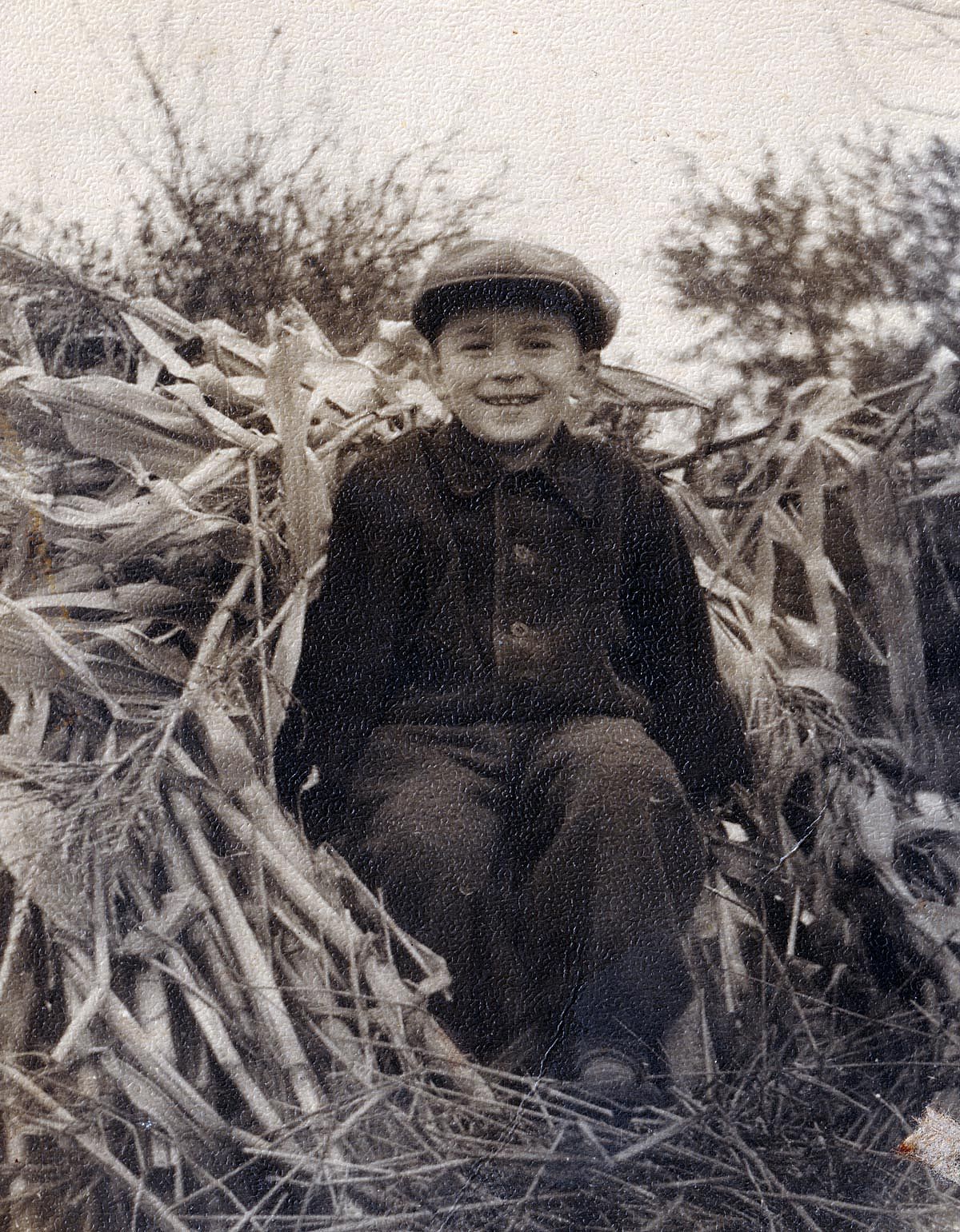 Black and white photo of a boy in the 1940s sitting in some corn husks