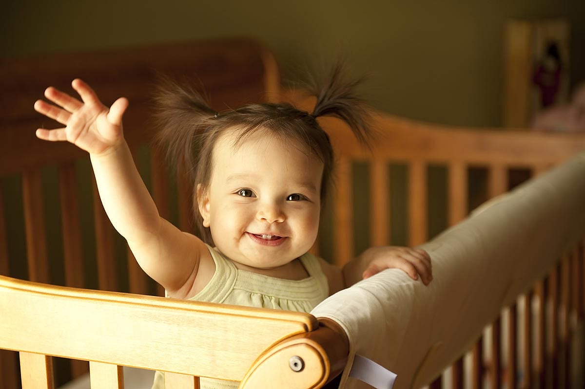 Little baby girl in a crib smiling and waving