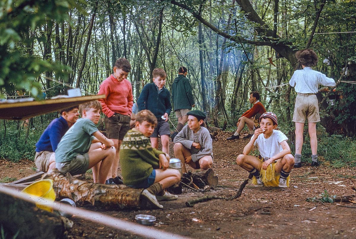 Beautiful color photo of some kids sitting around their campsite.