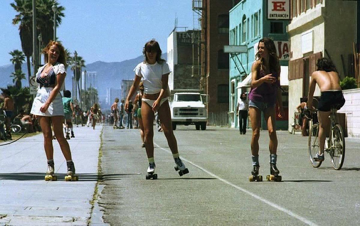 Three women rollerskating near in the beach in California, 1979