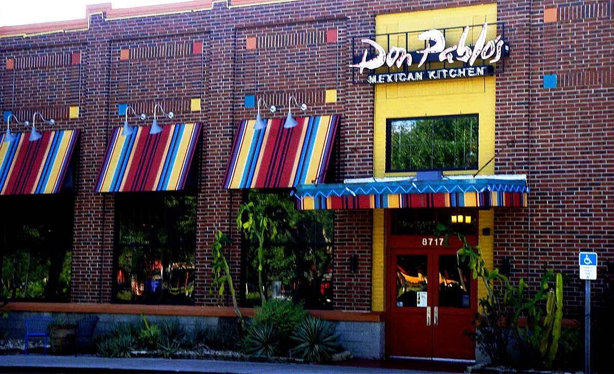 Exterior of a Don Pablo's Mexican Kitchen restaurant with colorful striped awnings and a brick facade.