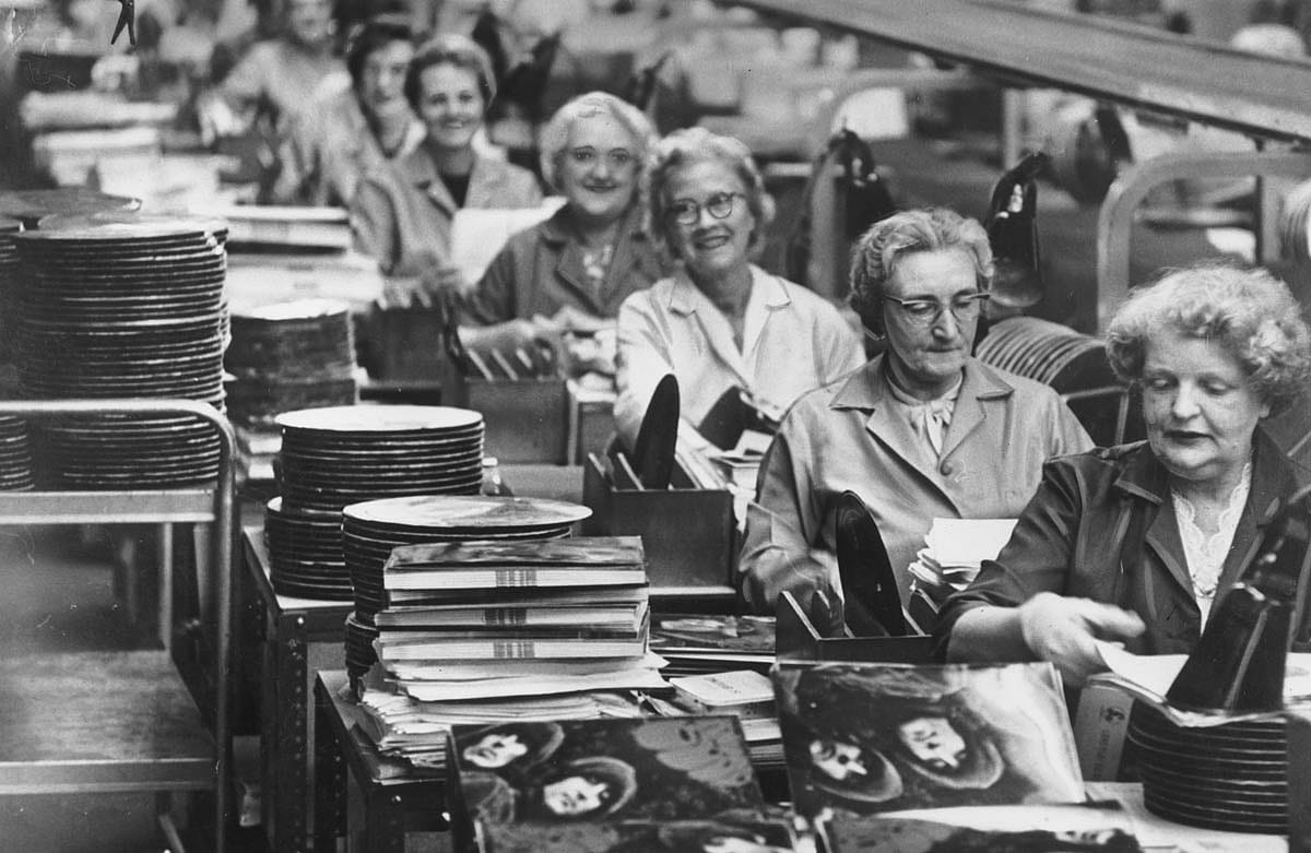 Women sit on a production line at the EMI factory, assembling the new Beatles record.