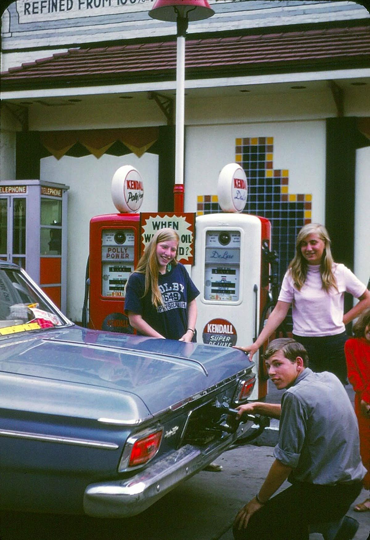 Two young girls pose while a young man fills up their gas tank.