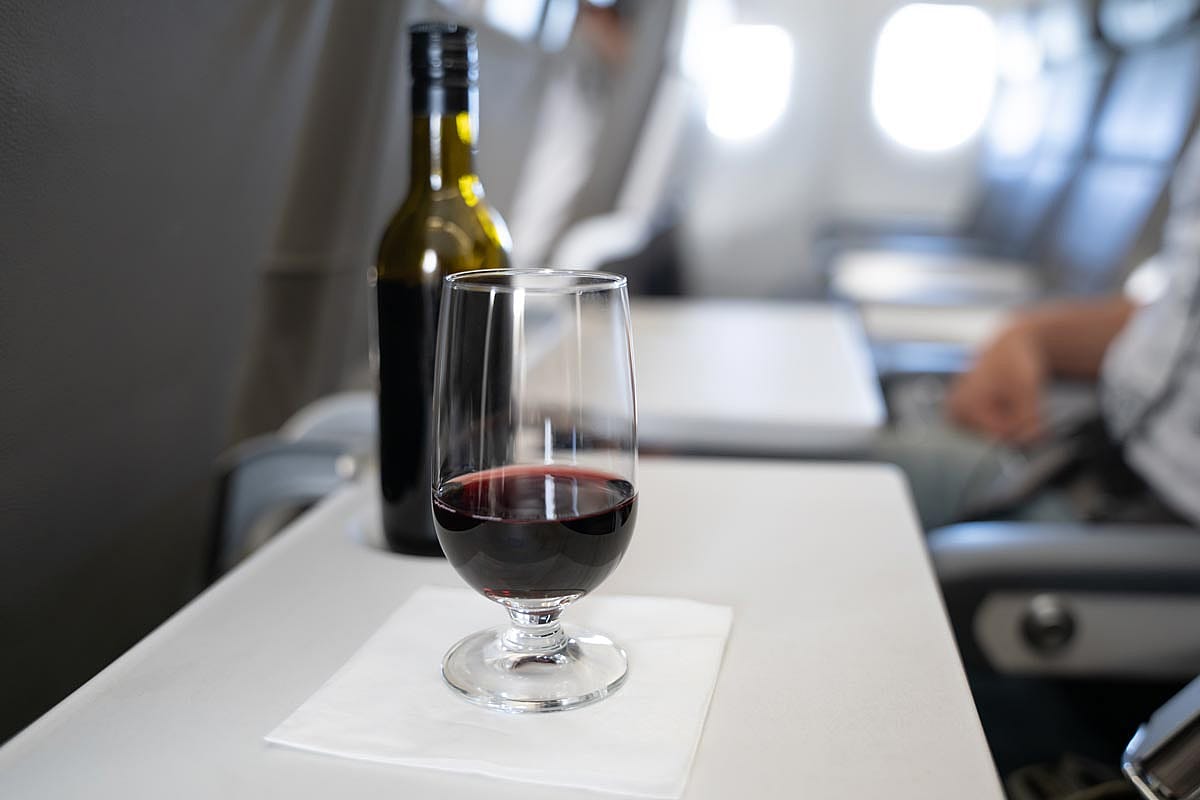 A glass with red wine and a small bottle in the background on the folding tray on an airplane