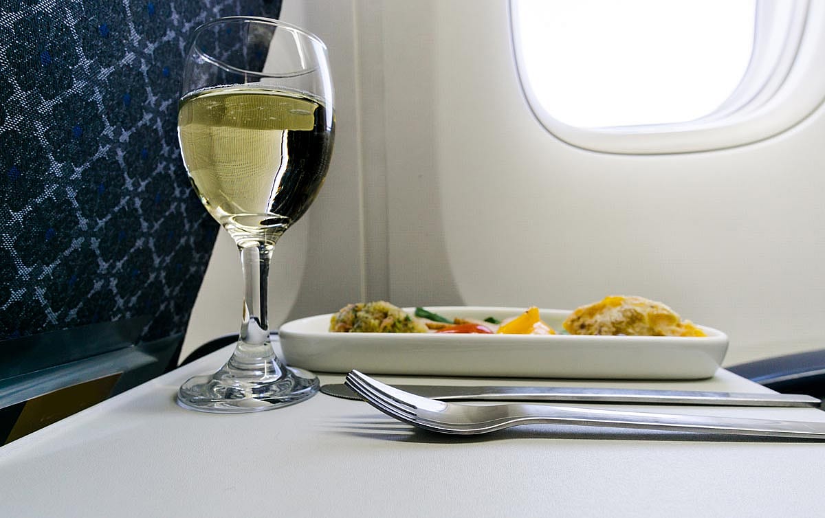 A glass of wine on a folding tray on an airplane.