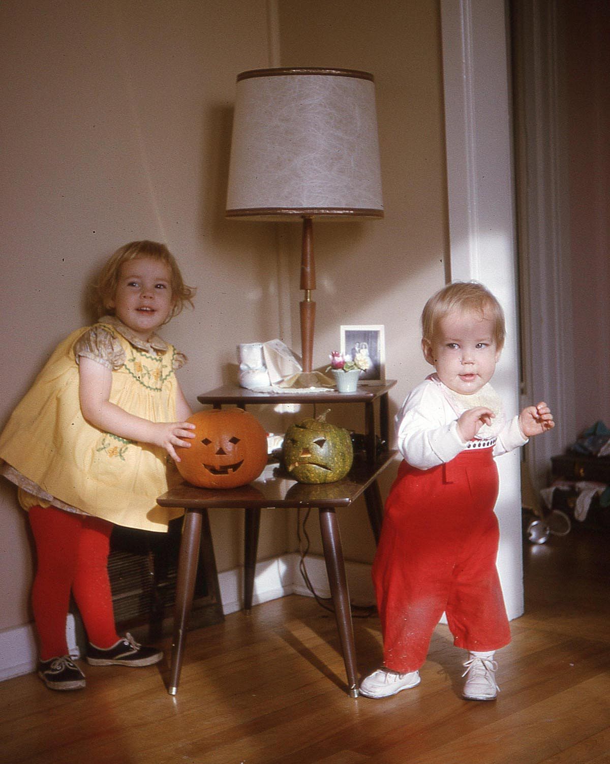 Beautiful color photo of two kids on halloween next to their pumpkins.