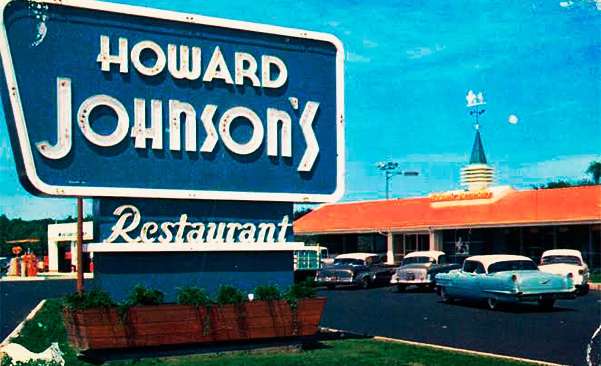 Vintage Howard Johnson's restaurant with its iconic roadside sign, orange roof, and classic cars parked outside.