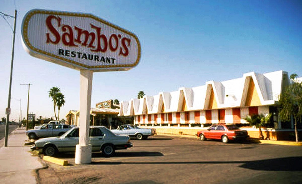 Exterior of a Sambo's restaurant with its large roadside sign, distinctive A-frame roofline, and cars parked in the lot.