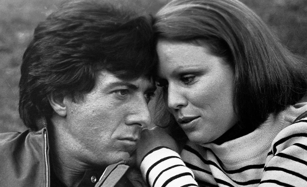 Dustin Hoffman and a woman share a quiet, intimate moment in a black-and-white scene from Marathon Man (1976), resting their heads together outdoors.