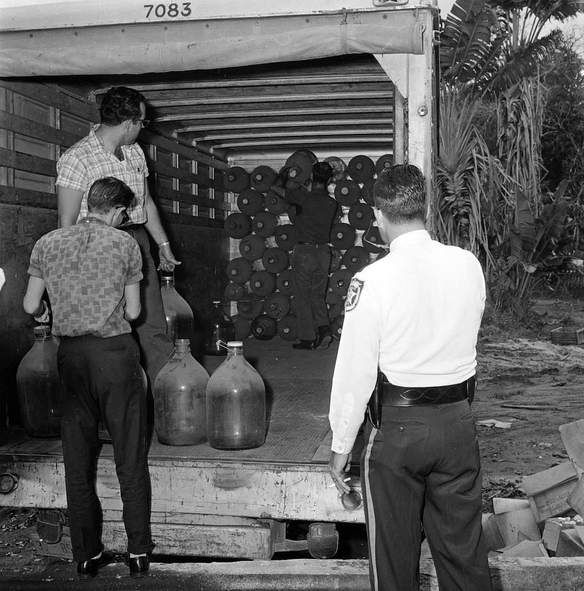 Black and white photo of a police officer and three men in the back of a moving truck filled with moonshine.
