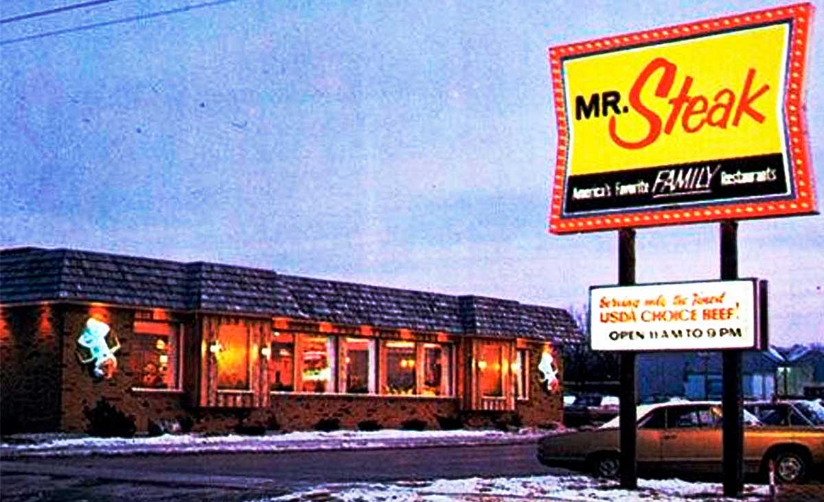 Vintage Mr. Steak restaurant at dusk with an illuminated roadside sign and snow-covered parking lot.
