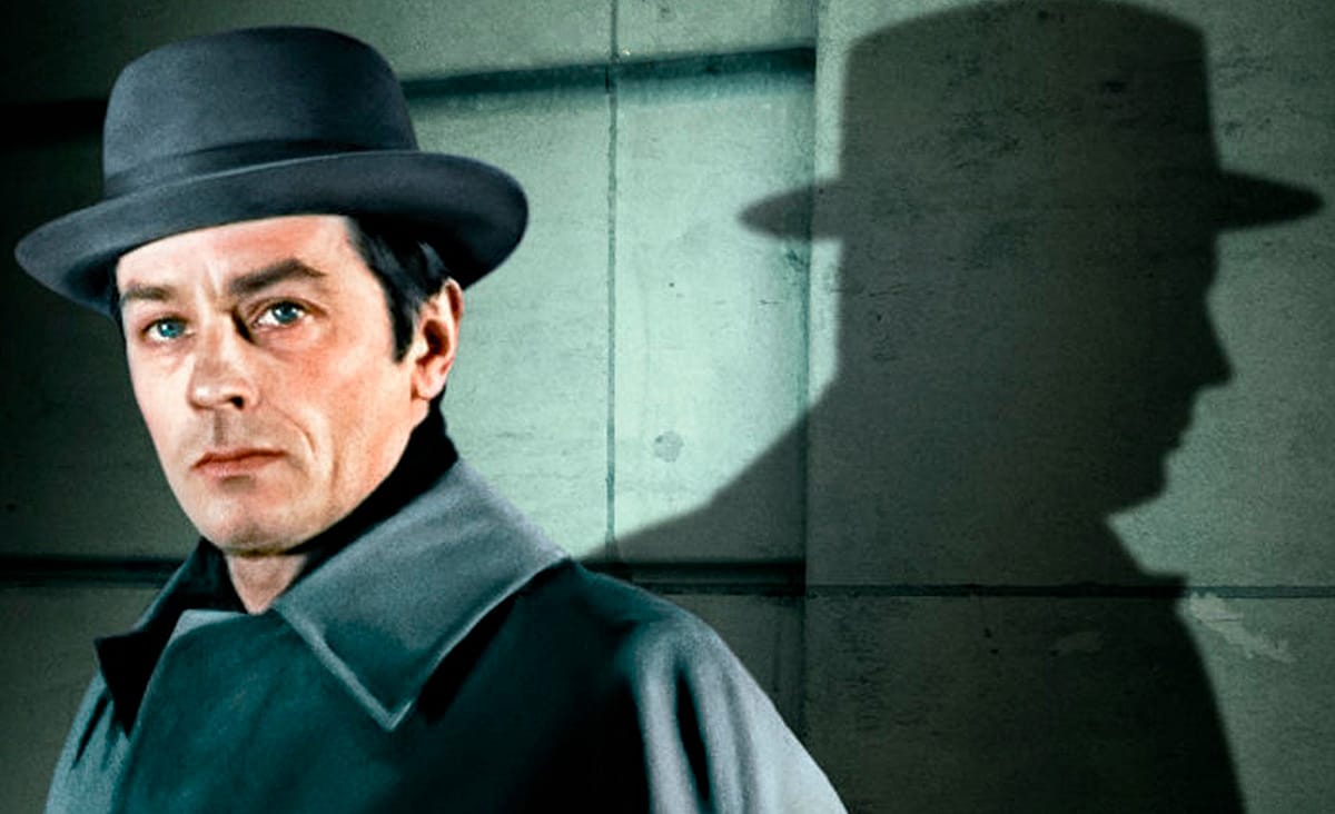 Alain Delon as Robert Klein in Mr. Klein (1976), wearing a gray coat and bowler hat, with his silhouette projected onto a wall behind him.