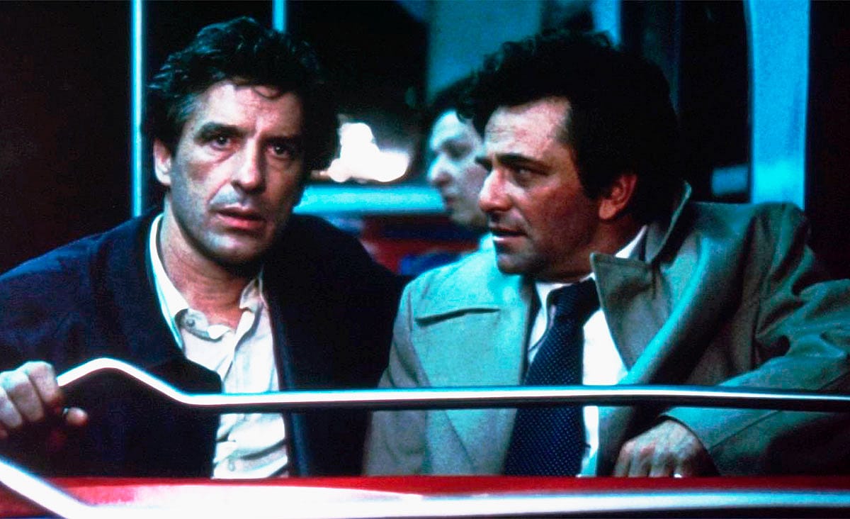 John Cassavetes and Peter Falk in Mikey and Nicky (1976), seated side by side on a nighttime bus, sharing a tense moment under dim blue lighting.