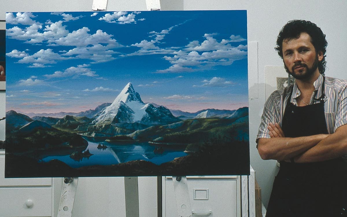 A man in a painter's apron posing next the Paramount Logo that he just painted.