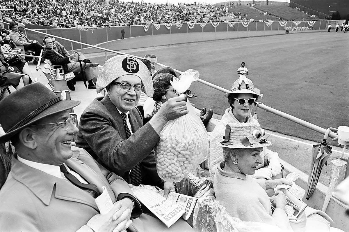 These fans arrived at the San Francisco Giants home opener prepared with plenty of peanuts, umbrellas for on-again-off-again showers, and zany hats at Candlestick Park in San Francisco, Calif. on April 20, 1965.