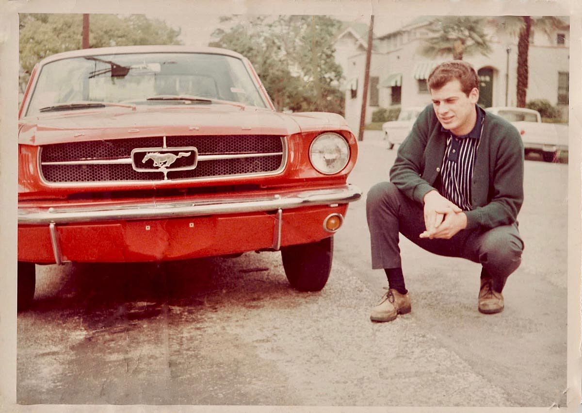 A man crouched down next to his new, red Ford Mustang.