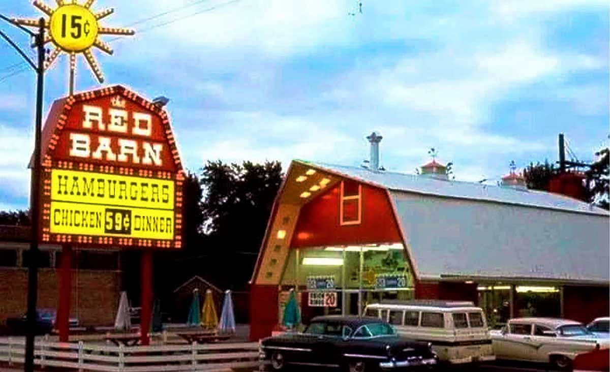 Vintage Red Barn fast-food restaurant with its signature barn-shaped building and illuminated roadside sign advertising hamburgers and chicken dinners.