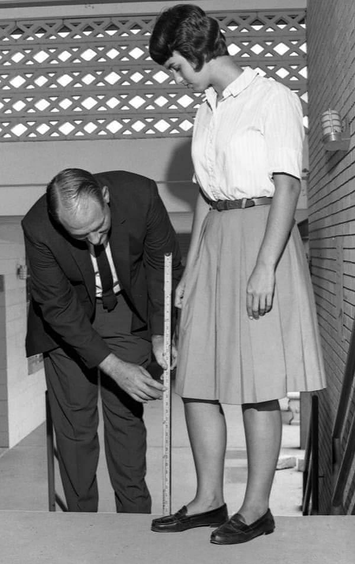 A man holding up a yard still to a students skirt.