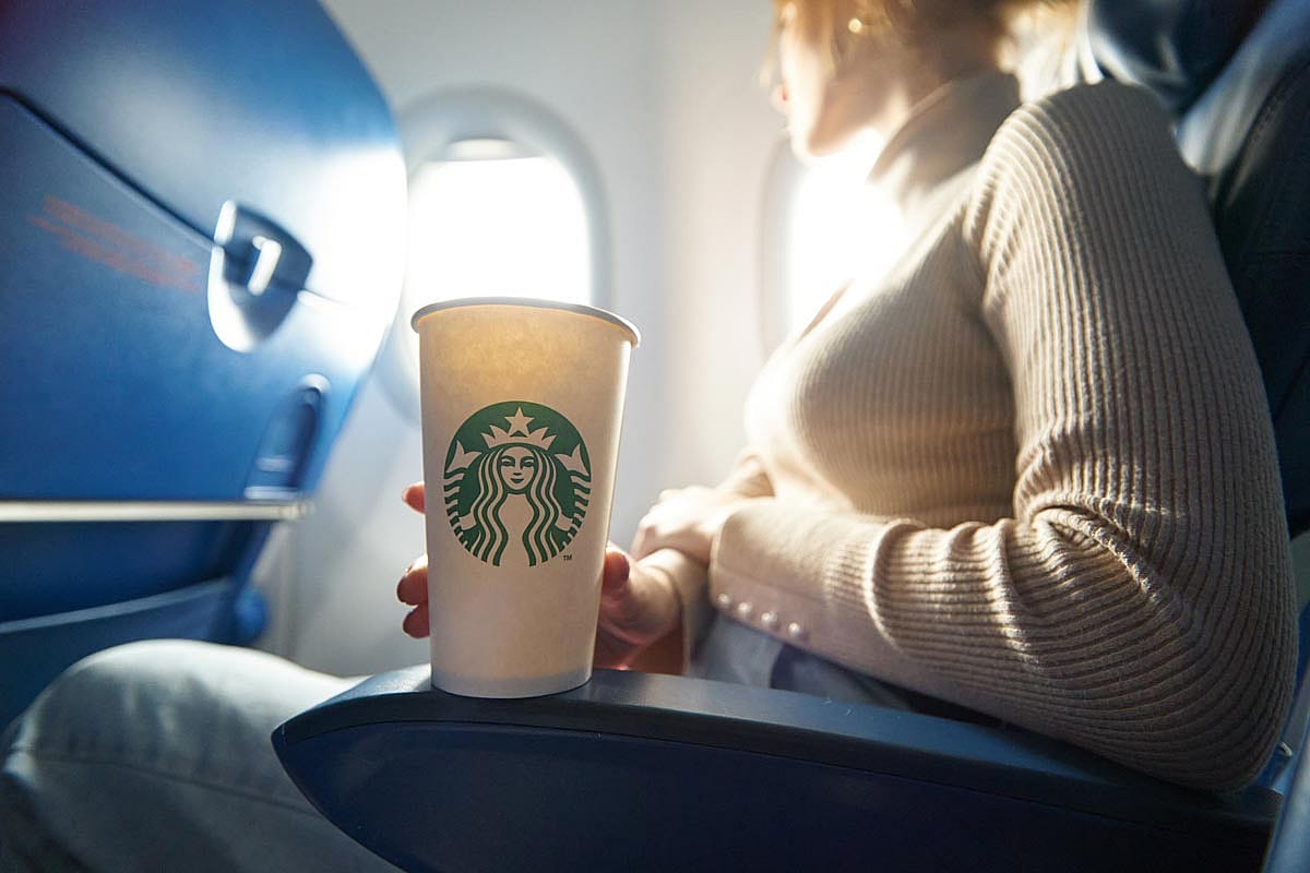 A woman on an airplane holding a Starbucks cup.
