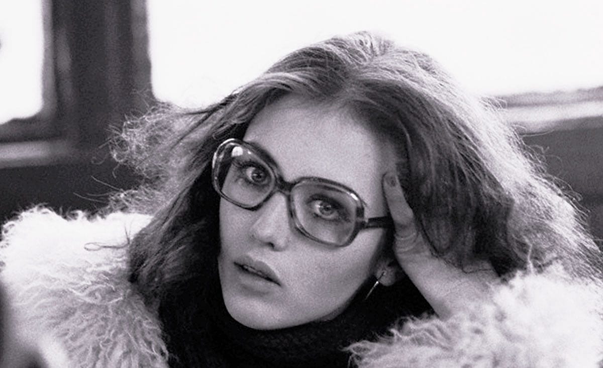 French actress Isabelle Adjani in The Tenant (1976), wearing oversized eyeglasses and a fur coat while resting her head on her hand in a black-and-white close-up.
