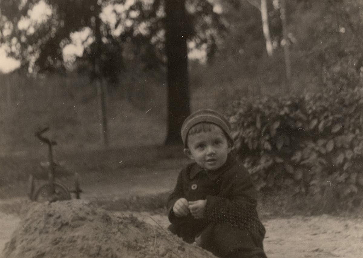 Vintage photo of a cute child playing near a sand pile. Old black and white photo yellowed with time. 