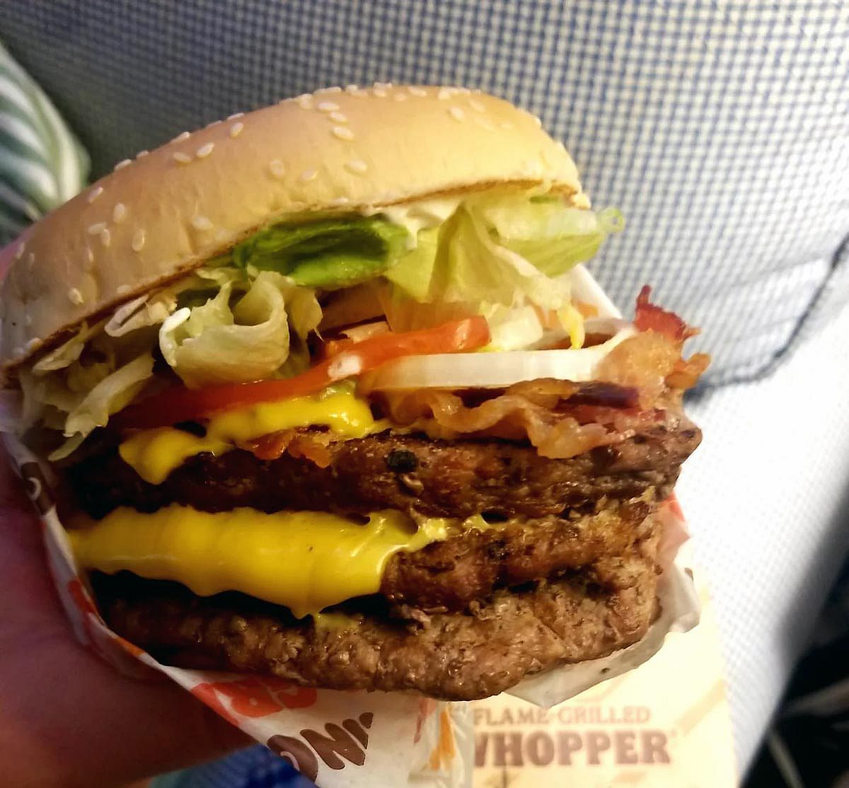 Hand holding a Triple Whopper with bacon and cheese from Burger King