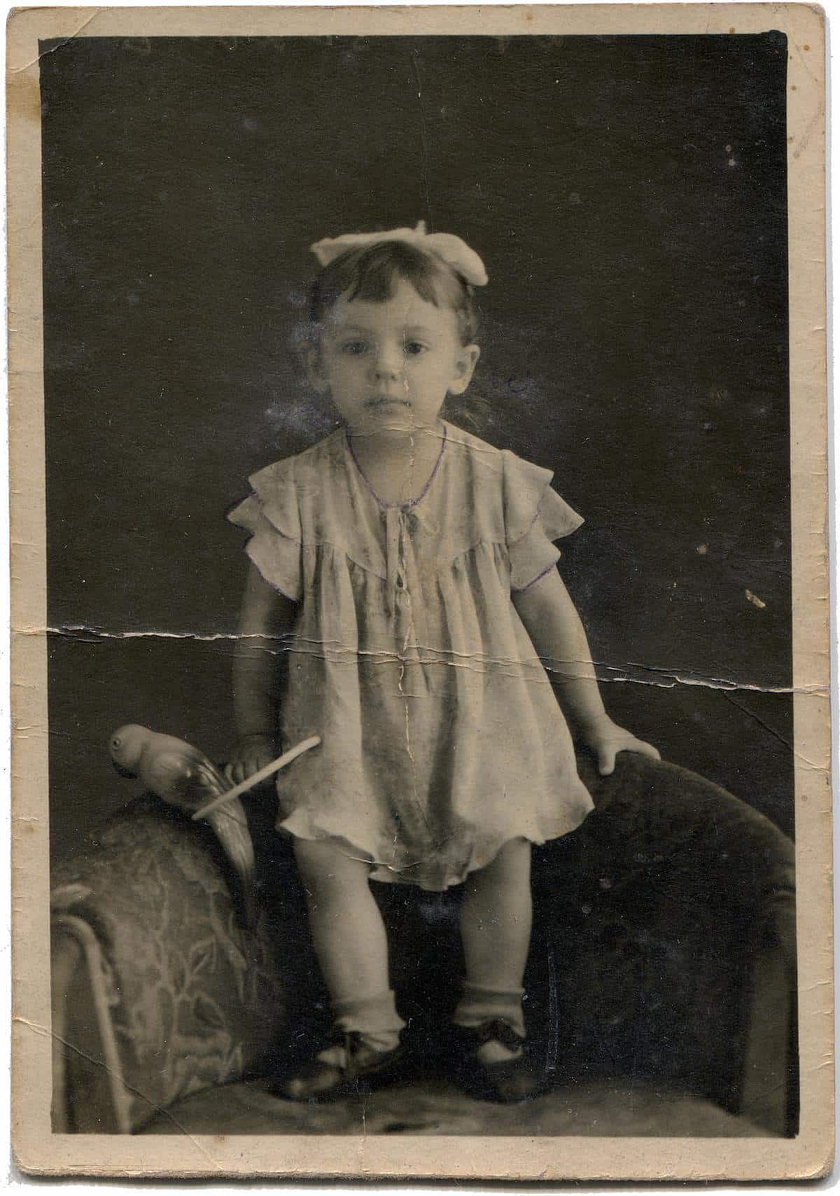 Vintage photo shows studio portrait of little girl staying on the armchair.
