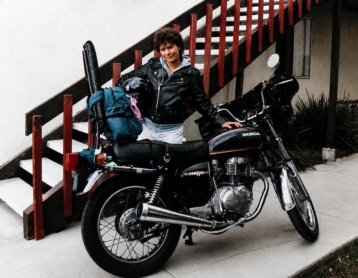A girl holding her motobike, wearing a leather jacket and a helmet, ready for the road.