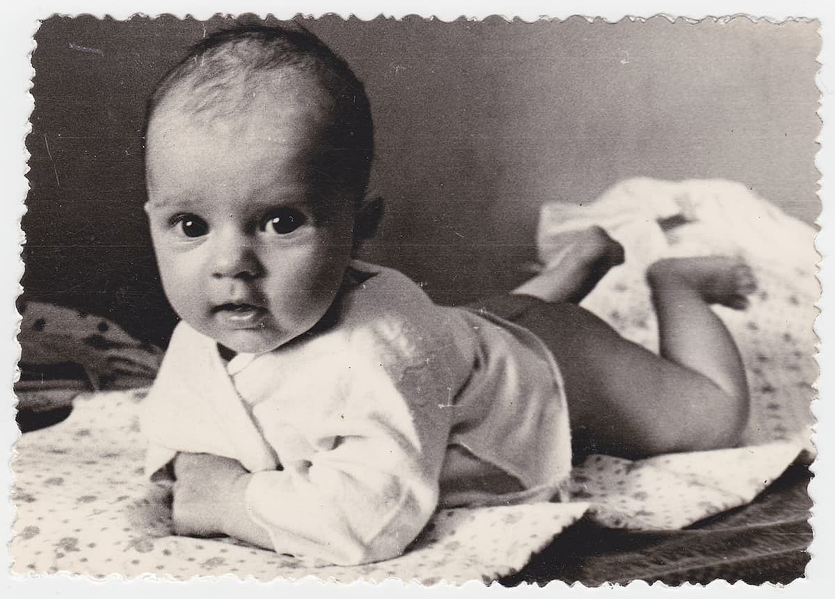 An old cute photo of a baby in an apartment. Vintage black and white photo, slightly yellowed by time, taken in the USSR around 1960.