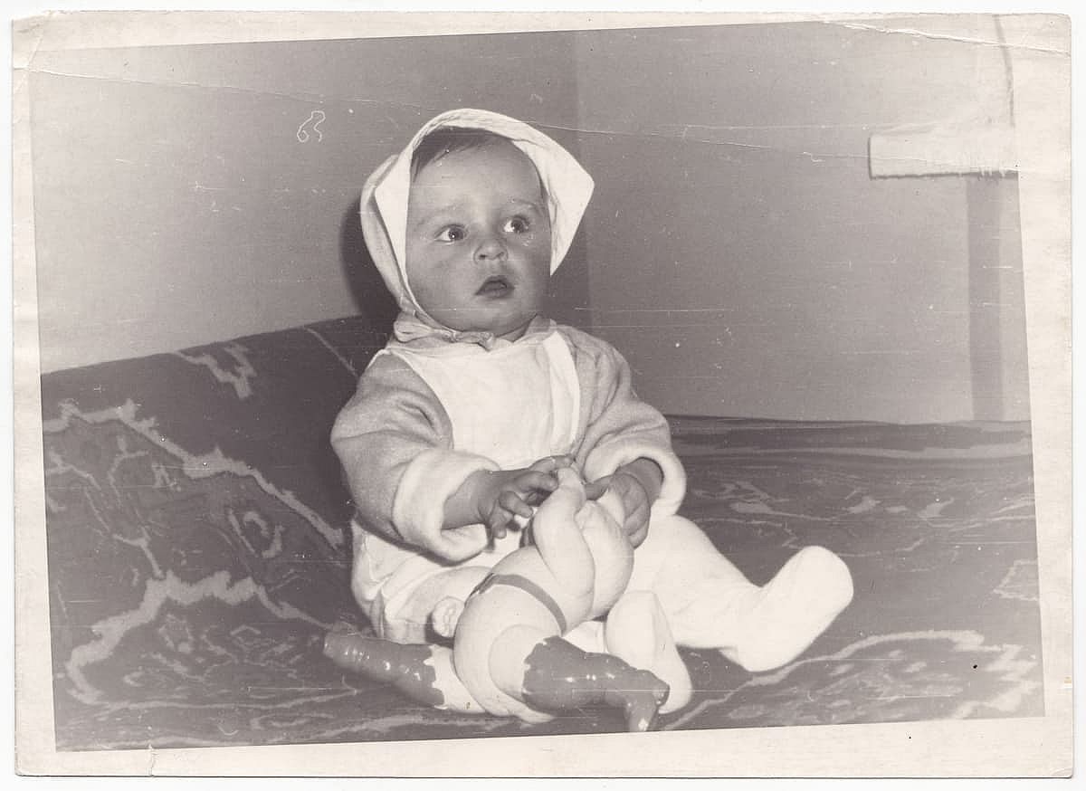 A cute baby in a crib in a vintage black-and-white photograph. This old, slightly yellowed retro photograph was taken in the USSR in the 1960s.