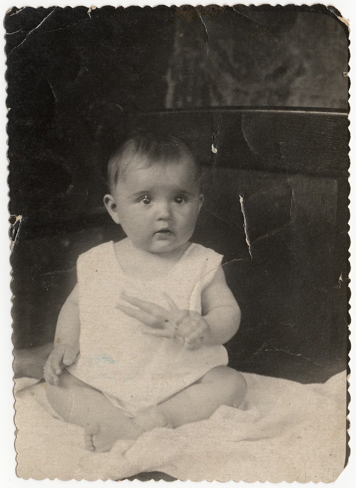 An old sweet photo of a cute baby sitting on a blanket. Vintage black and white photo, slightly yellowed with age.
